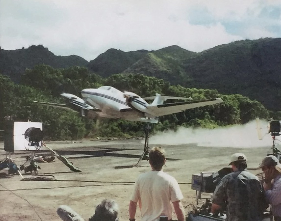 Twin-engine King Air performing ultra-low pass over jungle airstrip camera crew
