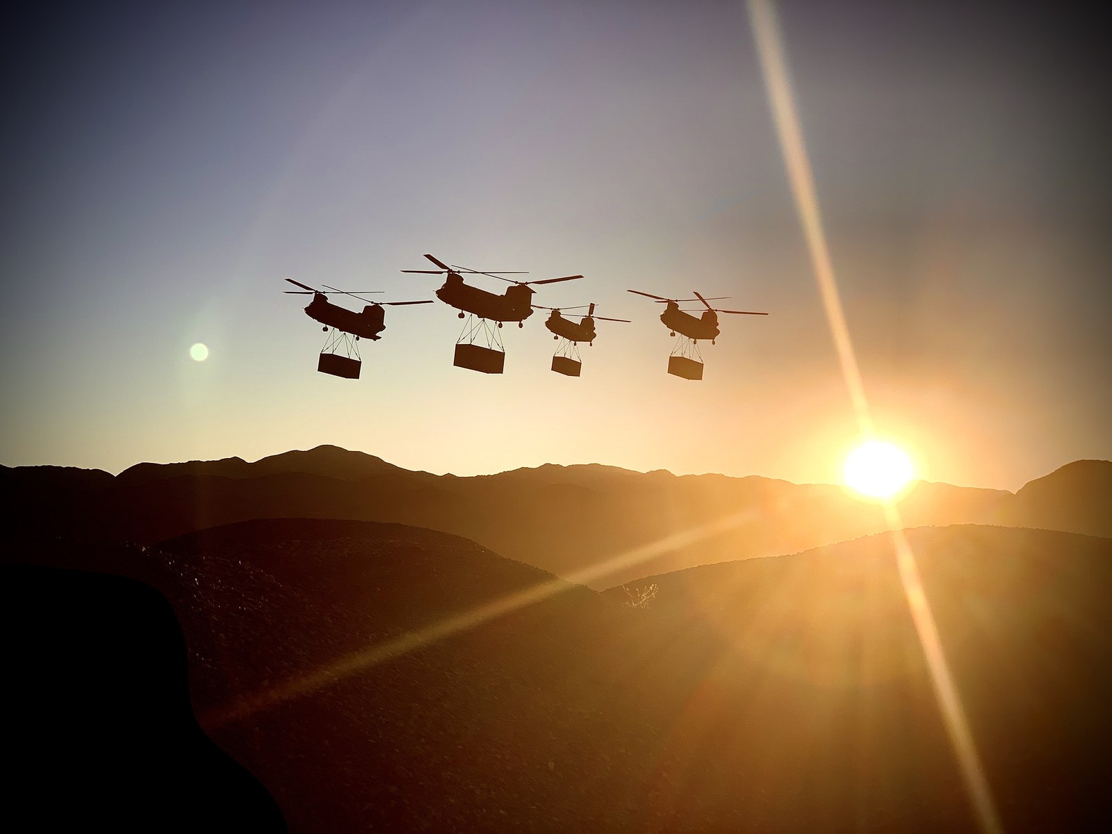 Four Chinook helicopters carrying sling loads at sunset for Tenet