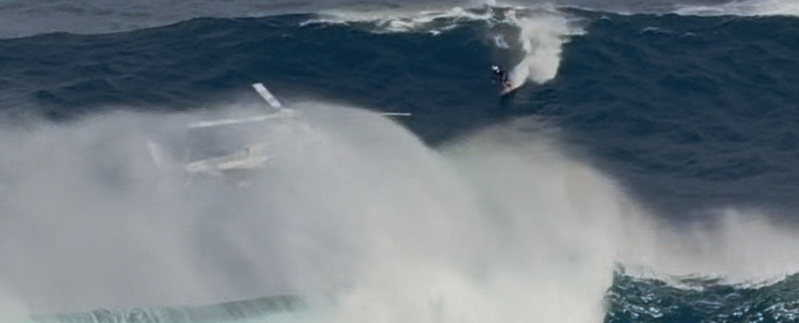 Camera helicopter flying inside giant ocean wave spray filming surfer